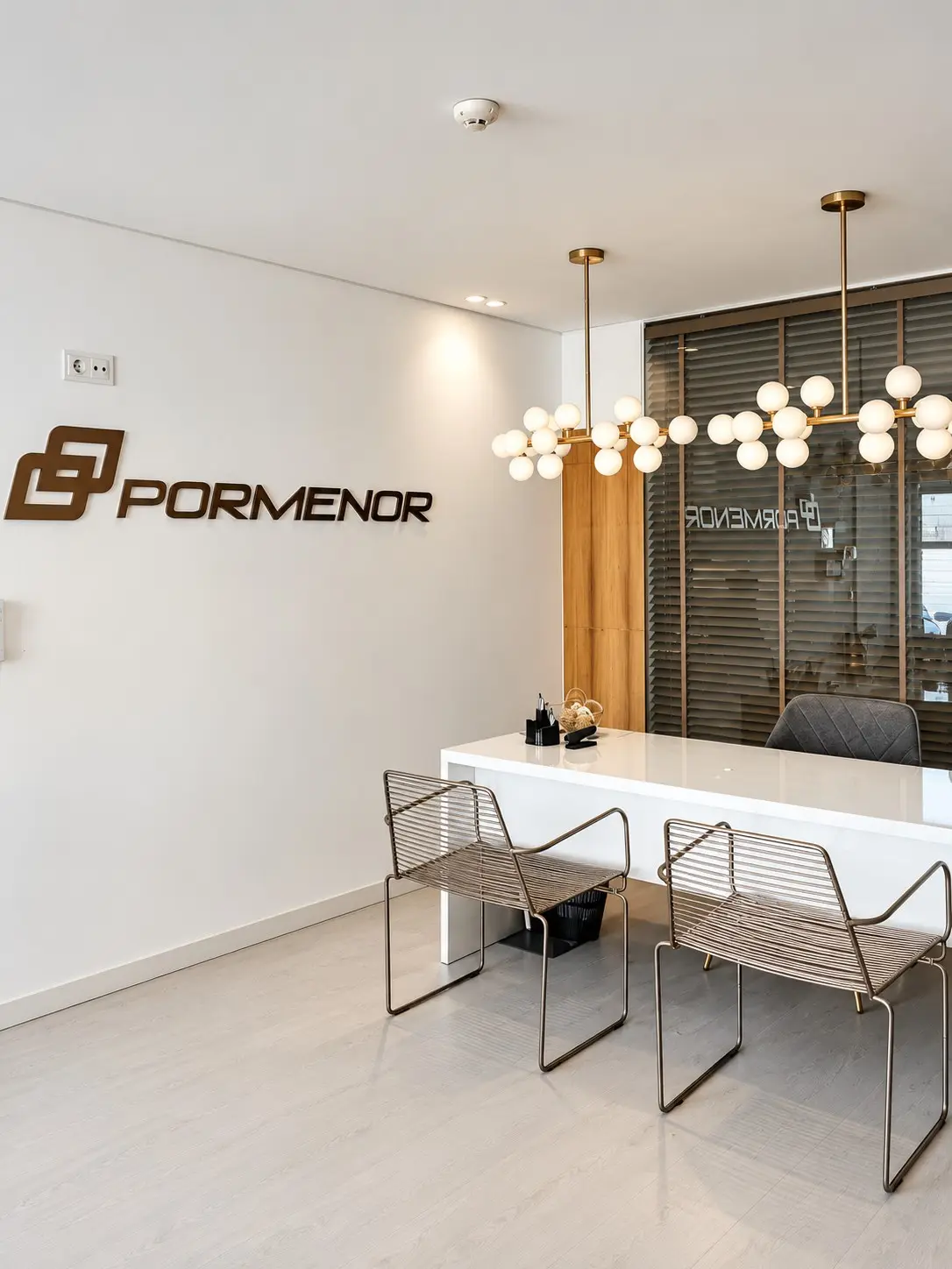 Receção da Pormenor, com balcão branco, duas cadeiras e candeeiros de globos